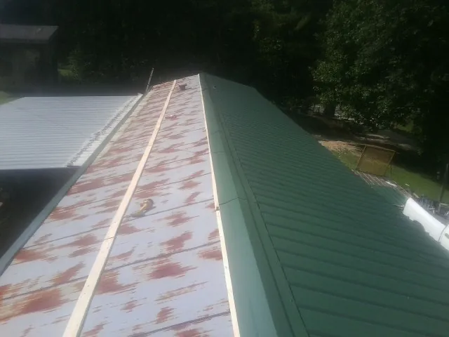 Old rusted panels beside newly installed green metal roofing — Wind Damage Roof Repair by Roofing Brothers in Adair