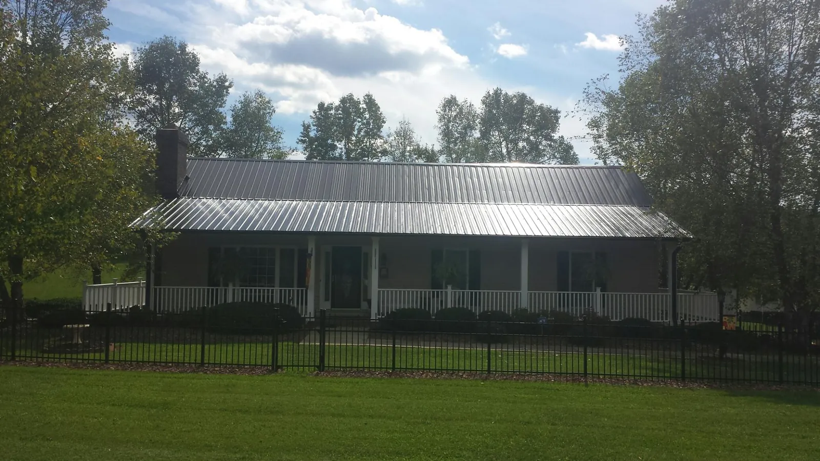 Gray metal roof on a brick ranch with a full width front porch — Gutter Guard Installation work by our crew in Adair