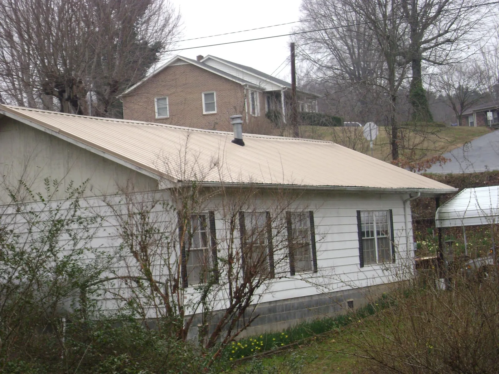 Tan metal roof on a white sided house set into a hillside — Commercial Roofing by Roofing Brothers in Adair