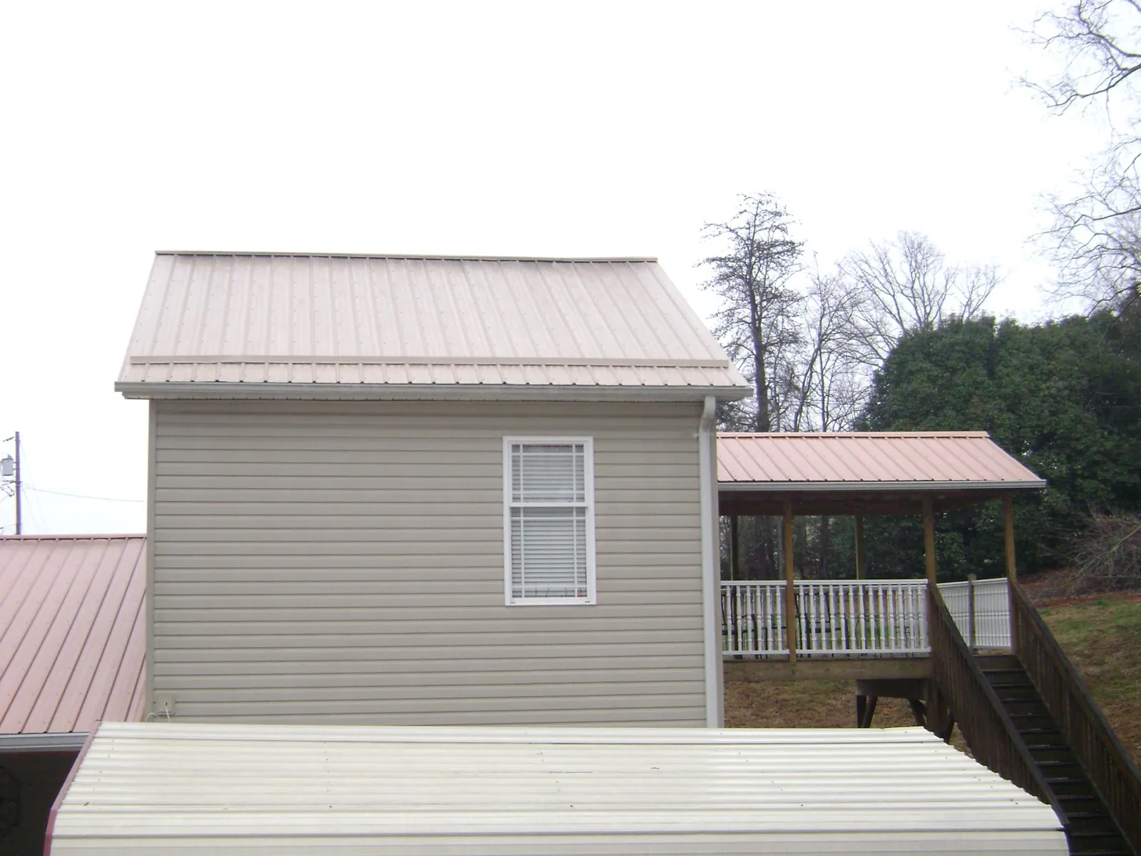 Tan metal roofs on a two story addition and attached porch, from a Roof Replacement job in Adair